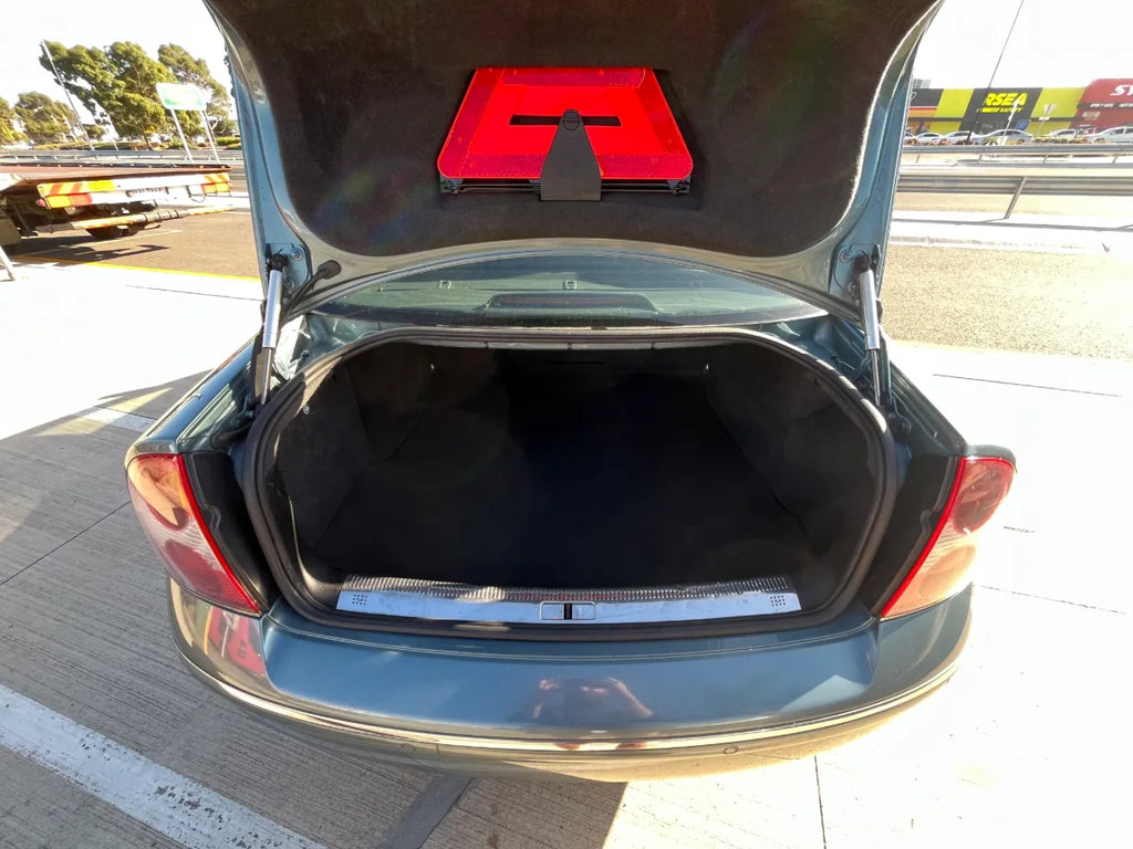 Open car trunk with a red and black object on a road.
