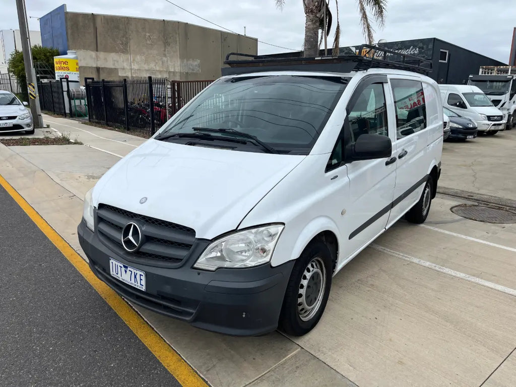 White Mercedes-Benz van parked on a street with a building and palm trees in the background.