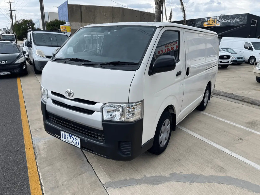 White Toyota van parked in a parking lot with other vehicles and buildings in the background.