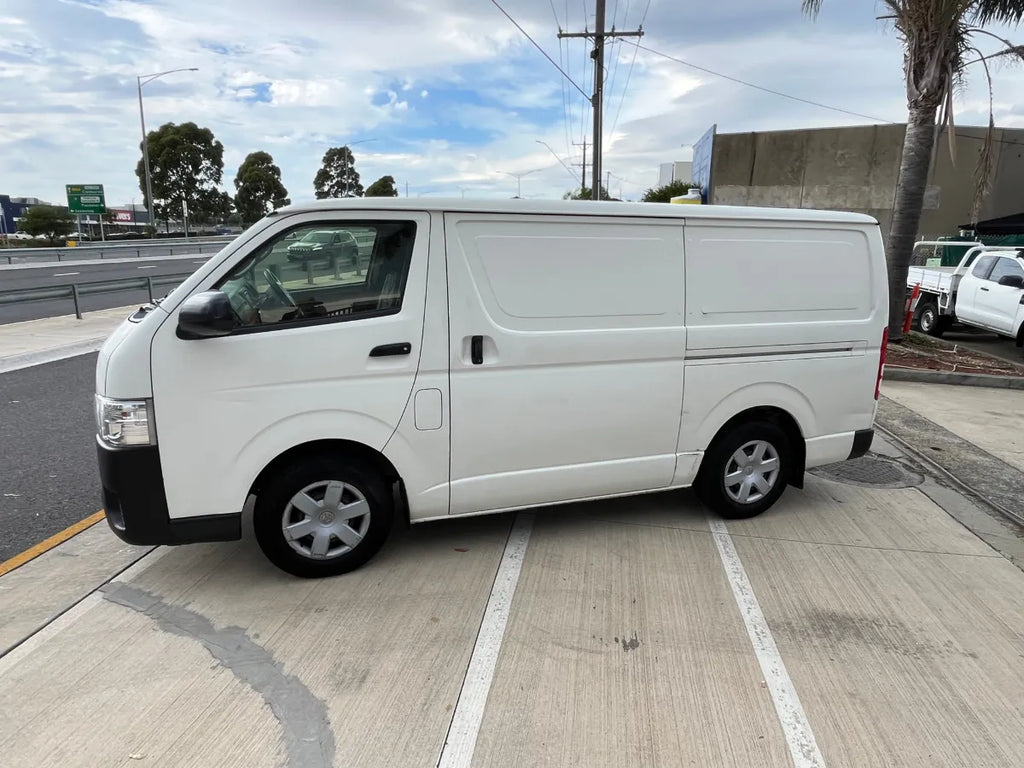 White van parked on a street with a clear sky and trees in the background