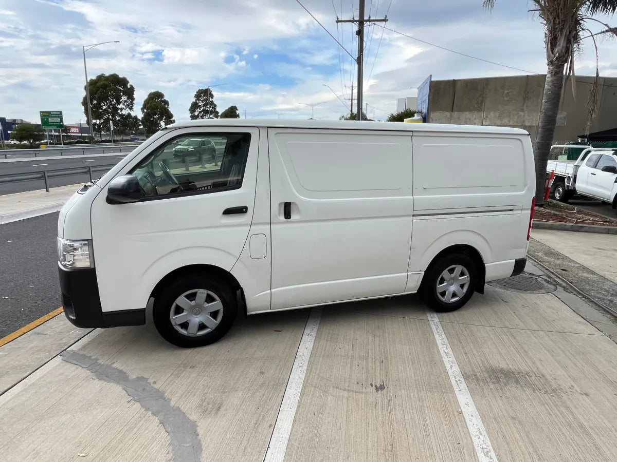 White van parked on a street with a clear sky and trees in the background