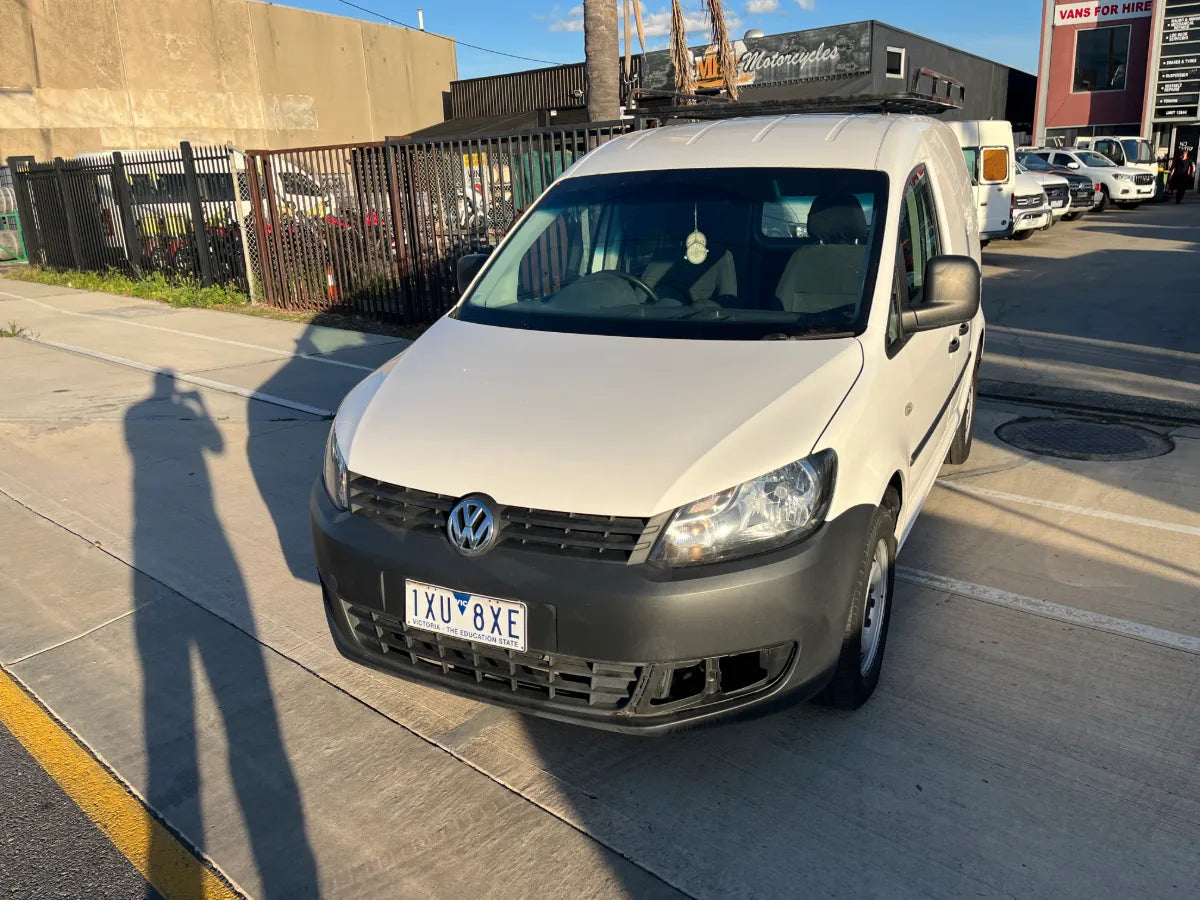 White Volkswagen van parked on a street with a person taking a photo, casting a shadow.