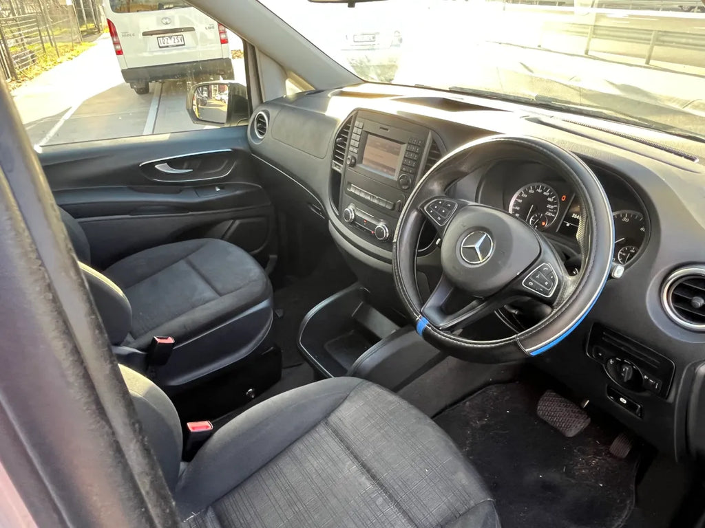 Car interior with steering wheel and dashboard, showing a Mercedes-Benz logo.