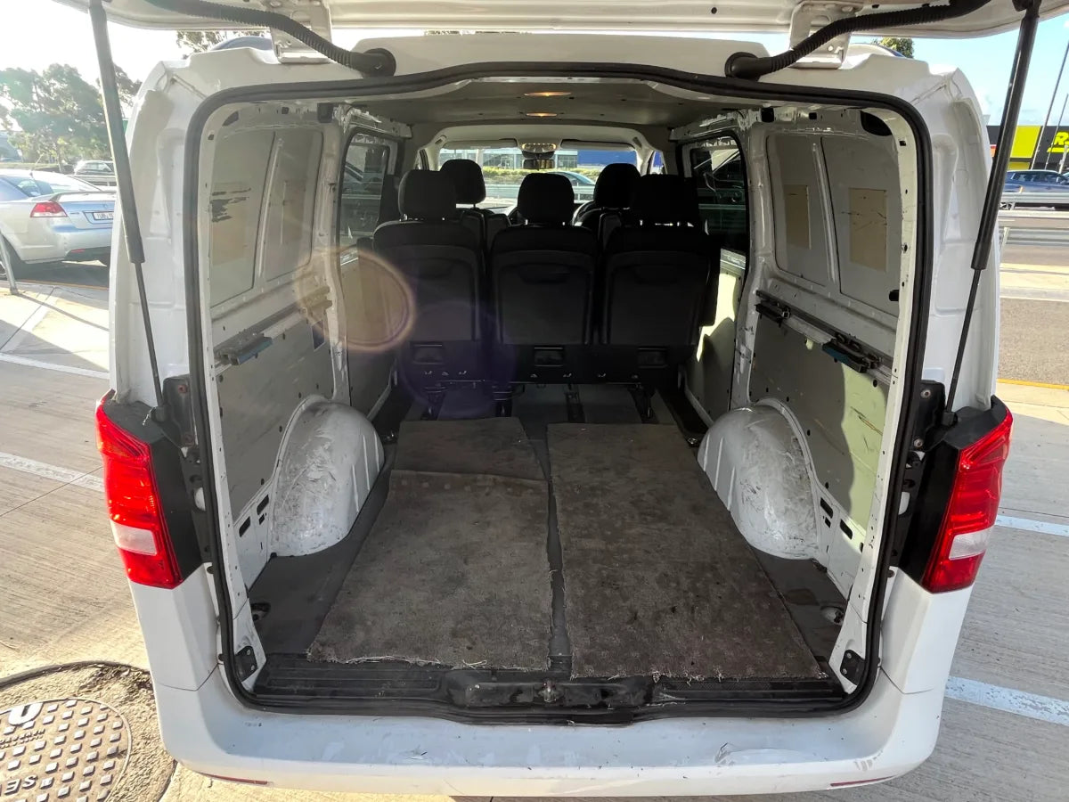 Back of a white van with open doors and seats removed, showing an empty cargo area.