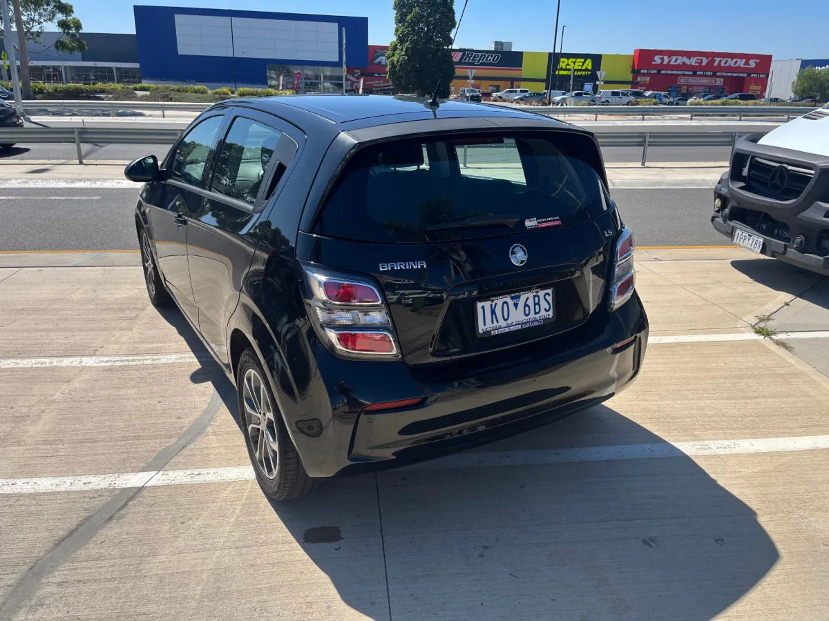 Black Holden Spark car parked on a road with a shopping center in the background